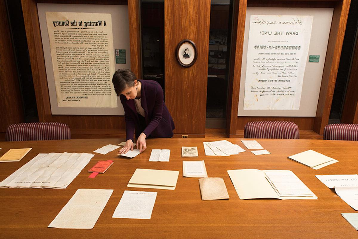 librarian at a large table arranges letters in front of posters about women's suffrage. 